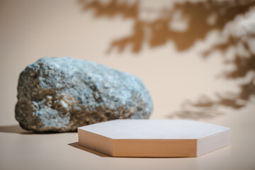 Creative concrete stone and beige platform podium for cosmetics or products with shadowes of greens branches on beige background. Front view