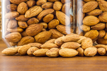 Almonds seeds pour from wood spoon on textured wooden background, top view.