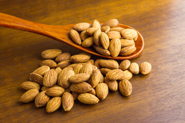 Almonds seeds pour from wood spoon on textured wooden background, top view.