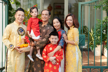 Smiling grandparents, parents and children in traditional ao dai dresses standing in front of house...