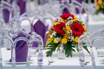 red - yellow - purple - white flower bouquet is set on the long white cover table and ready for luxury dinner in the garden field.