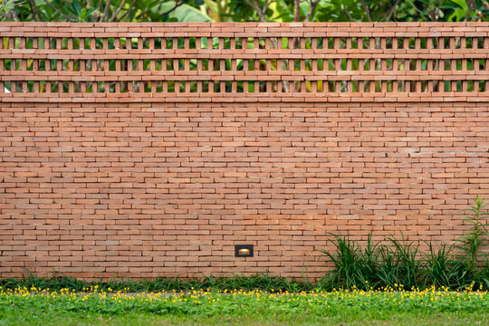 The brick wall, fence barrier is designed with a hole on top of wall in Asian style with garden grass field in the foreground