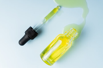 Face beauty oil spilled out of the dropper bottle on blue background. Concept of skin care serum. Unbranded product packaging