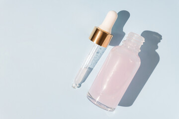 Top view of transparent dropper bottle with pink beauty face oil on blue background. anti aging serum with natural engredients.