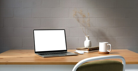 Computer laptop, potted plant, coffee cup and books on wooden table with brick wall.