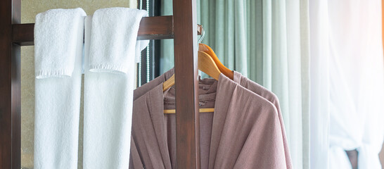 Closeup clean bathrobe and towel hanging in wooden wardrobe at luxury hotel. Relax and travel concept - obrazy, fototapety, plakaty