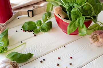 mortar with fresh basil and garlic on a light wooden table, space for text