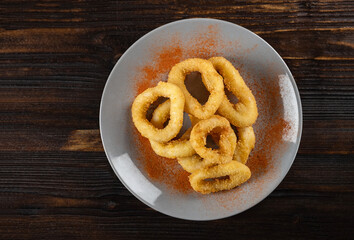 Beer appetizer from squid rings in batter in a plate on a wooden table. Top view, horizontal orientation, copy space, dark moody