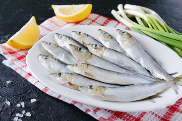 Fresh sea small fish on a plate on a concrete background. Sardines ready for cooking with lemon, coarse sea salt and green onion.