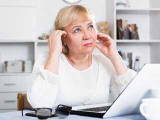 Mature woman sitting at home in front of laptop at table