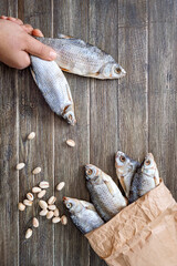 Hand holds several dried carp. Salty fish and pistachios on a wooden background. Traditional beer snack. Vertical view