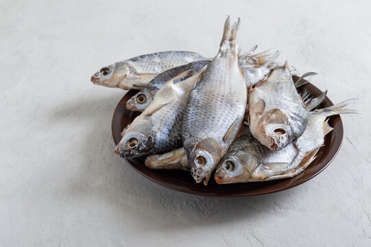 Dried salty river fish in a bowl on a light concrete background.