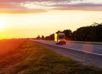 A van transports cargo on a motorway in the summer against the backdrop of a sunny sunset in the evening. The concept of cargo transportation on vans, mobility and speed of cargo delivery. 