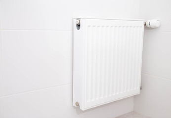 Modern wall-mounted heating radiator with thermostat on the white wall in the bathroom. Comfortable bathroom temperature, copy space for text