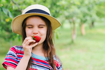 Little kid girl eating red strawberry in nature. Child enjoys a delicious berry.