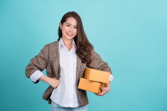Beautiful Asian businesswoman is happy in her work clothes holding a cardboard box. Delivery courier and shipping service concept.