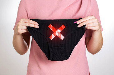 The girl is holding panties with a red cross. Concept of diseases of the female reproductive...