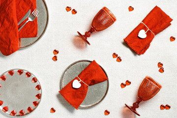 Creative pattern, festive table setting for Valentines Day romantic dinner with two red glass wine glasses, fashion plates, hearts as decoration, linen napkins on table, geometric pattern