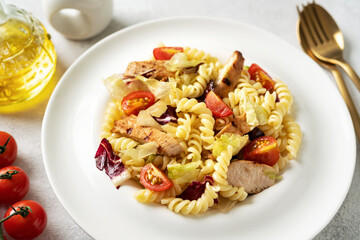 Pasta salad with grilled chicken, tomatoes and olive oil in a plate on a light culinary background. Traditional Italian dish girandole or fusilli fried poultry fillet and vegetables closeup	