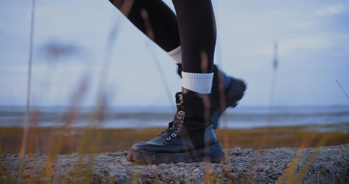 Closeup woman boots steps by seashore early morning