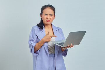 Portrait of sad young Asian woman pointing fingers at a laptop and looking at camera isolated on white background