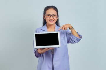 Portrait of smiling young Asian woman pointing fingers at a blank screen of a laptop, with copy space for presenting product isolated on white background