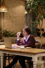 Fototapeta premium Focused businesswoman, writer or journalist work in cafe use laptop and wifi internet connection. Concentrated afro american female in headphones listen to webinar training courses during coffee break