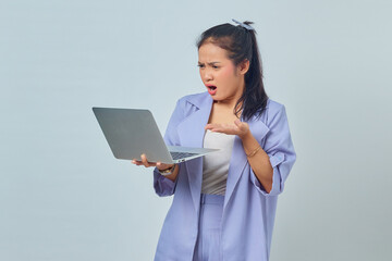 Portrait of angry young Asian woman showing copy space in palms and holding laptop isolated on white background
