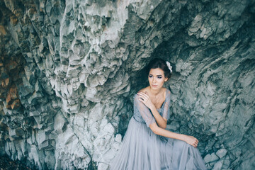 Beautiful brunette bride in a gray dress of tulle and lace near the rock.
