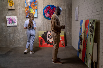 Young African man with leaflet standing in front of creative artwork while visiting modern art...