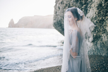Beautiful brunette girl bride in a grey gown of lace and tulle, covered her face with a veil, hand on breast,