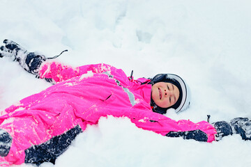 Cute happy girl snowboarder in bright winter clothes spends time in a snowy snowboard park. Smiling...