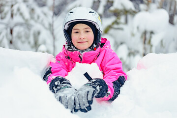 Fototapeta na wymiar Cute happy girl snowboarder in bright winter clothes spends time in a snowy snowboard park. Smiling girl of caucasian ethnicity on winter outdoor recreation. Fun in the snow