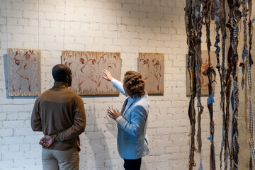 Contemporary artist presenting to young African male visitor one of his artworks hanging on wall in...