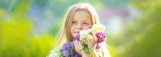 Fototapeta premium Banner with spring kids portrait. Little girl in the garden with long fair hair being excited to get a bouquet of lilac on a birthday.