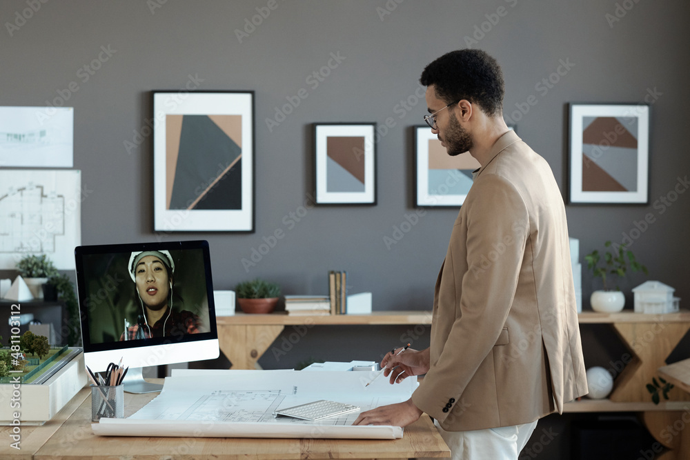 Poster young biracial engineer in formalwear looking at female builder on computer screen during online dis