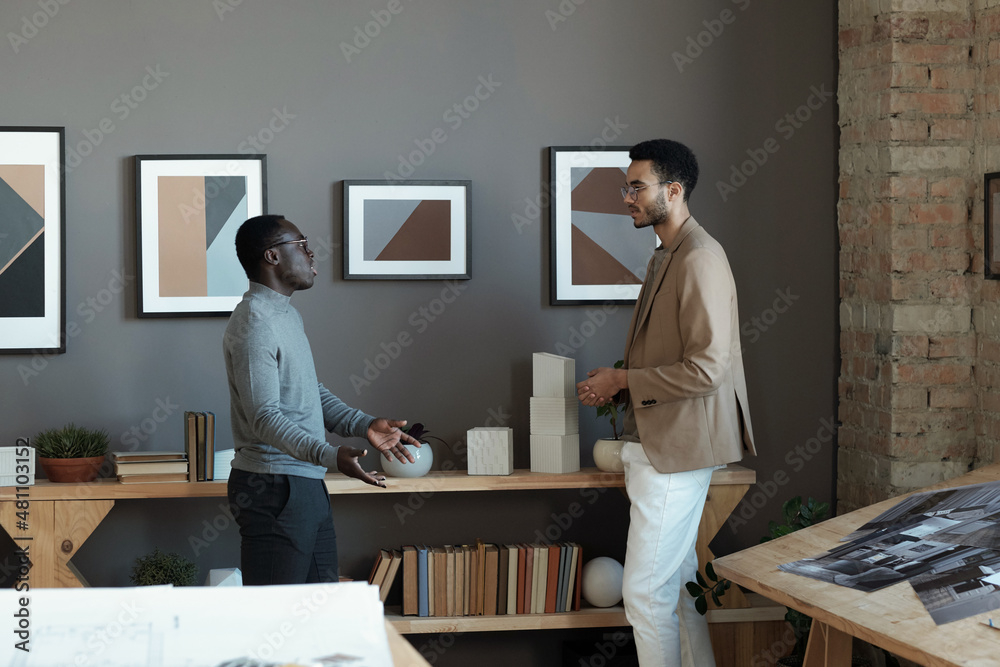 Aufkleber Two young intercultiral businessmen discussing working points while standing in front of each other against wall with paintings
