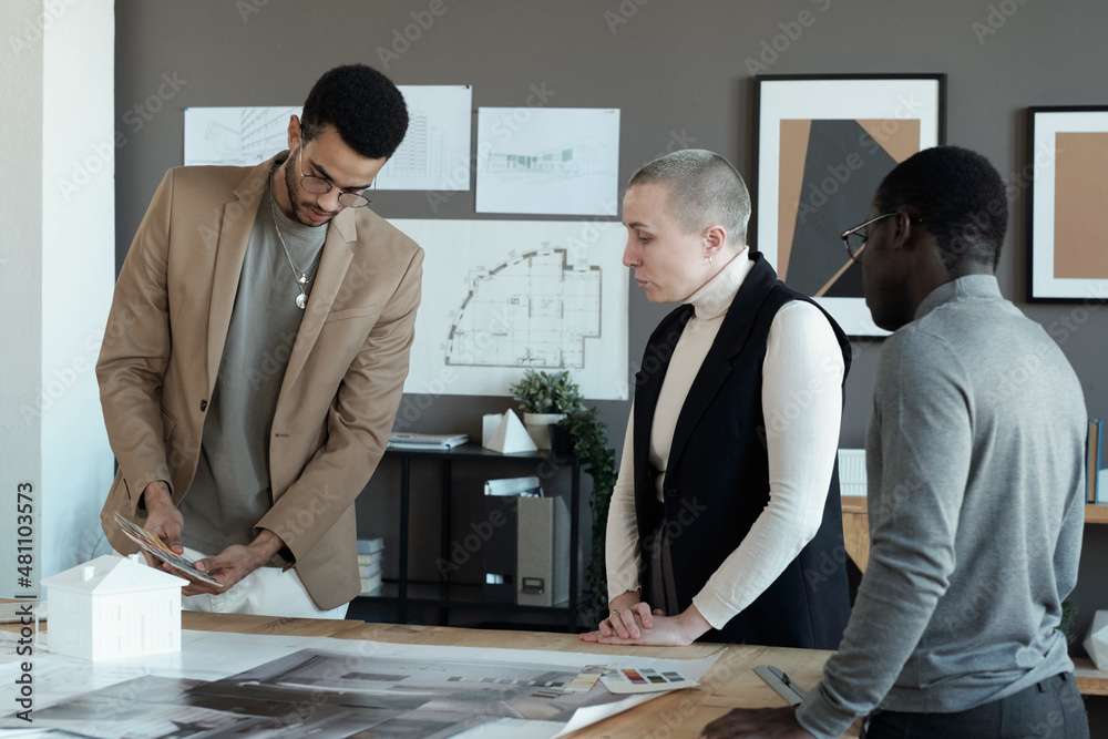 Poster young biracial male designer showing color palette to colleagues while discussing and choosing swatc