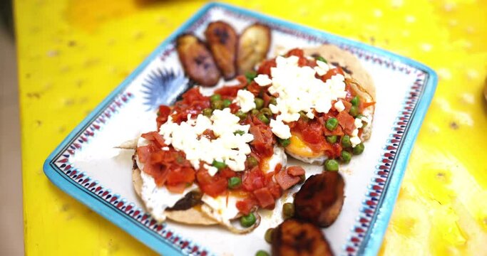 Plate of huevos rancheros and fried banana slices on yellow surface