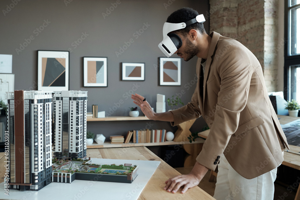 Poster Young elegant architect in vr headset standing by table with house layout during presentation of his new project