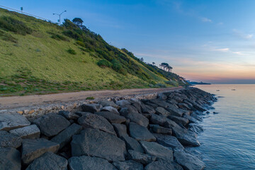 Breakwater and grassy hill with trees at sunset in Frankston, Australia