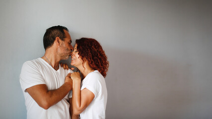 Cute European middle-aged couple tender hugs against a gray wall. Man and woman together, support. gray plain background, copy space