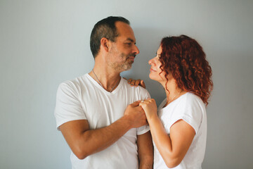Cute European middle-aged couple tender hugs against a gray wall. Man and woman together, support....