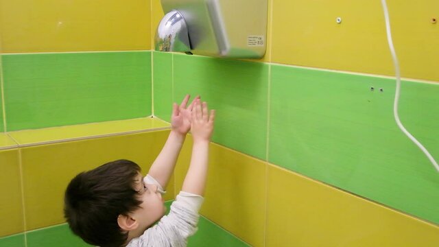 A boy of 3-4 years old dries his hands with an electric automatic dryer