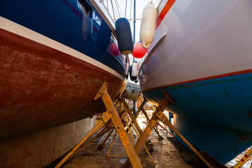 Sailing yachts are in dry dock and supported by metal supports.