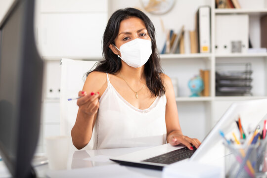 Hispanic female office employee in medical face mask conducting meeting in office. Concept of social distance in work during coronavirus pandemic..