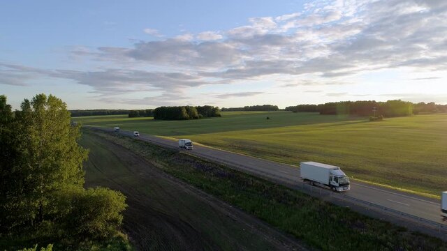 Aerial view of trucks and cars driving on an intercity road between green fields in the beautiful morning of summer day