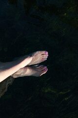 Lifestyle photo of bare feet legs with trendy pedicure of pastel colors in the water on sunny summer day. Relaxing in nature concept.