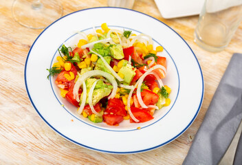 Popular all over the world appetizing vegetable salad of tomatoes, avocado, canned corn and onion, cut into rings