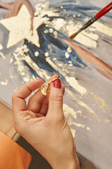 female hands transfer the gold potal to the picture, layering it with a brush